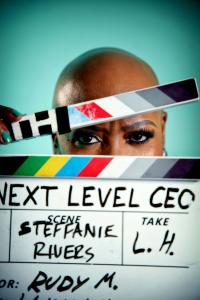 Close-up photograph of Steffanie Rivers looking through a film clapperboard marked NEXT LEVEL CEO during television production.