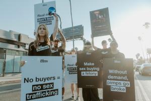 Protestors hold signs in the street, demanding accountability for sex buyers