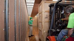 An Arnoff supervisor in a green uniform points to a stack of crates inside a large truck, while an employee operates a forklift nearby.