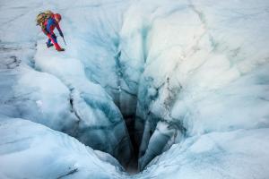 ICE-SAR-Rettungskraft in roter Einsatzkleidung nähert sich einer tiefen Gletscherspalte.