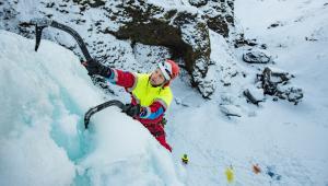 ICE-SAR-Rettungskraft beim Eisklettern mit zwei Eisgeräten in verschneiter Berglandschaft.