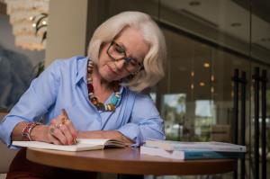 Psychotherapist and author Judy K. Herman writing in a notebook at a coffee shop table with her two relationship books beside her.
