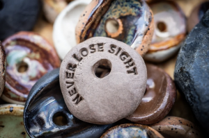 Pile of handcrafted clay Sight Stones, with one stone turned upside down to show “Never Lose Sight” stamped into the clay.