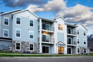 The Village on 4th apartment complex at dusk in Springville, Utah, highlighting illuminated balconies, stone exterior details, and mountains in the background under a cloudy sky.