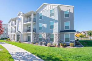 Modern apartment building exterior at The Village on 4th in Springville, Utah, featuring light blue siding, stone masonry, and private balconies under a clear blue sky.