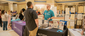 People engage at informational booths inside a building, including one for Autism Foundation of Oklahoma.