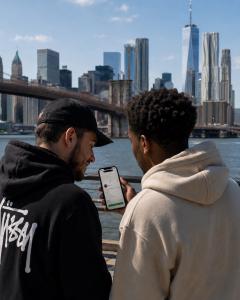 Two people looking at a Secret World app task listing on a phone with the New York City skyline behind them.