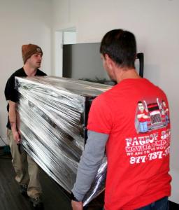 Two Fatboy Slims Moving Company movers carrying a shrink-wrapped dresser during a full-service move