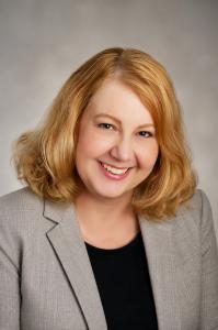 Professional headshot of author Kathy S Garrett smiling, wearing a grey blazer against a softly lit neutral background.