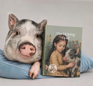 Photo of the minipig Hercules, posing with his book in the H.A.K. Heroes series, "The Helping Hoof"