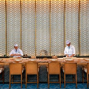 Two Japanese chefs preparing food behind a counter in an elegant restaurant.