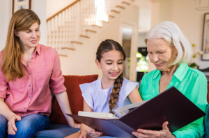 Older woman reading a book with a young girl and woman at home