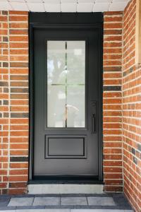 A newly installed modern black front door with a frosted glass window, set in a red brick exterior.