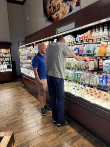 Two people are in the dairy section of a grocery store. One is helping the other organize milk on shelves.