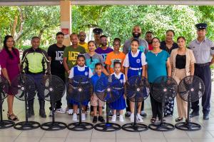 Gymnast Ali Coles stands with primary school students, staff and police officers behind a row of donated standing fans in Trinidad.