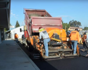 Commercial asphalt paving crew operating machinery for road and parking lot construction.