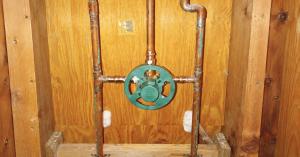 Copper plumbing lines and green shower valve inside open wall framing.
