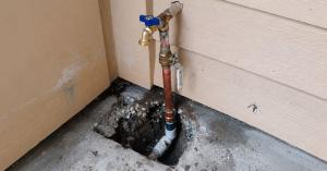Exterior copper water pipe and blue hose bibb against house siding.
