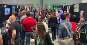 Crowded Small Business Expo exhibit hall with attendees talking at booths and a Business Card Exchange sign in the background.