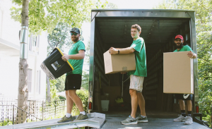 Three Horsepower Moving and Storage movers carrying boxes at the back of a moving truck.