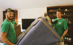 Two Horsepower Moving and Storage movers holding blanket-wrapped furniture with a cat perched on top.