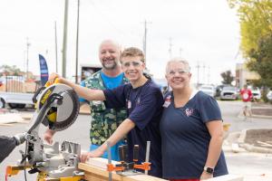 Sleep in Heavenly Peace (SHP), the leading national nonprofit dedicated to building and delivering beds to children in need, celebrated its eighth annual Bunks Across America (BAA) event that mobilized 17,761 volunteers with 232 chapters nationwide Sept A Lowe's associate helps a mother and her teenage son operate a miter saw at an outdoor bed-building event.