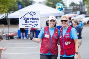 Two Lowe's associates in red service vests smile together, one holding a