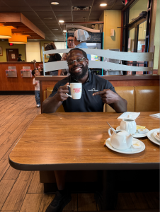 Carlos Puckerin, founder of Texas Roof Advisor, smiling while holding a coffee mug at a Houston-area restaurant.