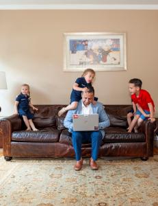 State Farm Agent Jacob Ayubi working on a laptop while his young children play around him on a sofa.