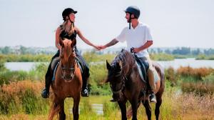 A smiling couple on horseback holding hands during an outdoor excursion near Falésia Hotel in the Algarve, surrounded by wetlands and greenery.