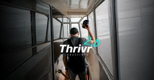 Videographer holding a camera and mic walks down a boat corridor, with the Thrivr Productions 2.0 logo overlaid.