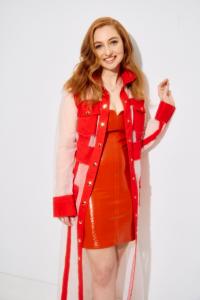 Singer-songwriter Ashley Ann in a red dress and sheer red-trimmed coat against a white backdrop.