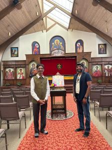 Hiten Bhuta standing with a community representative inside St. Mary’s Orthodox Church in Roswell, with the church interior and religious artwork visible in the background.