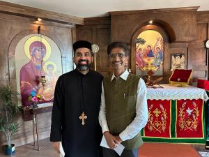 Hiten Bhuta standing with a church representative inside St. Mary’s Orthodox Church, with religious artwork and the church altar visible in the background.