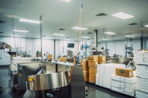 Wide view of automated capsule processing machinery and stacked product trays inside Vox Nutrition's cGMP supplement manufacturing cleanroom.