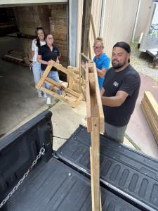 Three volunteers lift wooden bed frame pieces into the bed of a pickup truck.