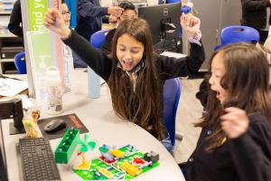 Two students celebrate with raised arms while working on a hands-on electronics project at a computer station in a SmartLab.