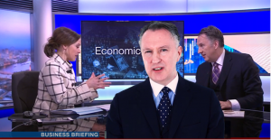 Screenshot of the Guildhawk Voice avatar or digital twin of David Clarke speaking in a multilingual video as his human twin is interviewed in a television news studio by a news presenter