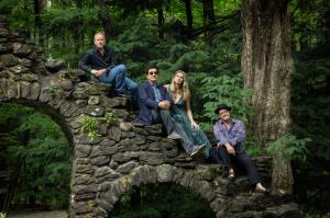 A female artist and three males sit on old ruins in a Vermont forest. 
