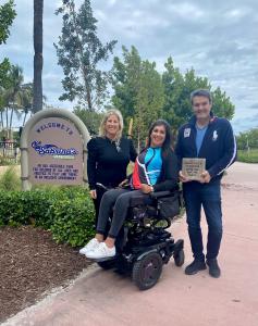 ALT="Hassan Jalali Bidgoli holds a paver to help build an inclusive walkway on Miami Beach. He stands next to Sabrina Cohen (in a wheelchair), founder of the Sabrina Cohen Foundation, and Stacey Glassman Mizener, executive director."