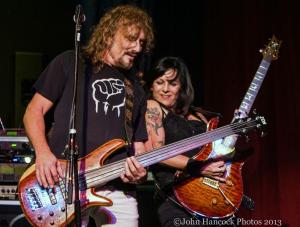 Rock musicians Lynn Sorensen on bass and Roni Lee on guitar performing on stage together.