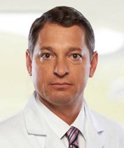 Greg Vigna headshot, wearing a white lab coat and tie