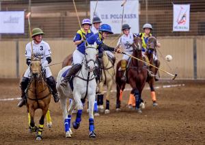 a woman on a horse playing arena polo hits the ball in the air