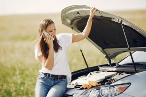 Woman on a smartphone standing next to a vehicle with the hood open