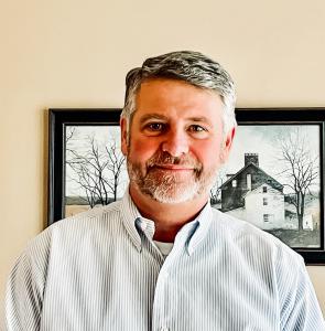 Wade Architectural Systems has hired Mike Lawes as Regional Sales Manager of the US Mid Atlantic Region man standing in front of a photo with a gray striped shirt and gray hair and beard
