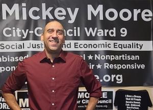 Mickey is best known as the man who battled the state of Minnesota to establish a viable and vibrant professional hair braiding industry Candidate Mickey Moore standing in front of campaign banners