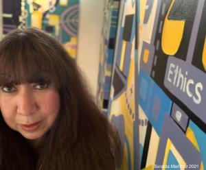 Photo of Artist, Soraida Martinez, with Verdadism Painting, Ethics, in Background.