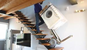 A man carries a washing machine up the stairs with an electric stair climbing dolly