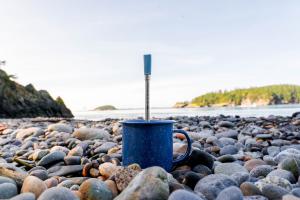JoGo Straw standing in a blue camping mug, which is sitting on the rocky beach of the Pacific Northwest.