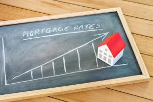 Graph representing the rise in mortgage interest rates drawn on a chalkboard lying on a wooden table. A model of a house with a red roof is on the chalkboard